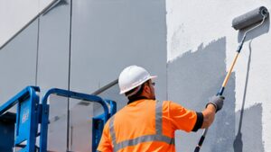 Professional painter wearing safety equipment applying paint to the exterior wall of a commercial building